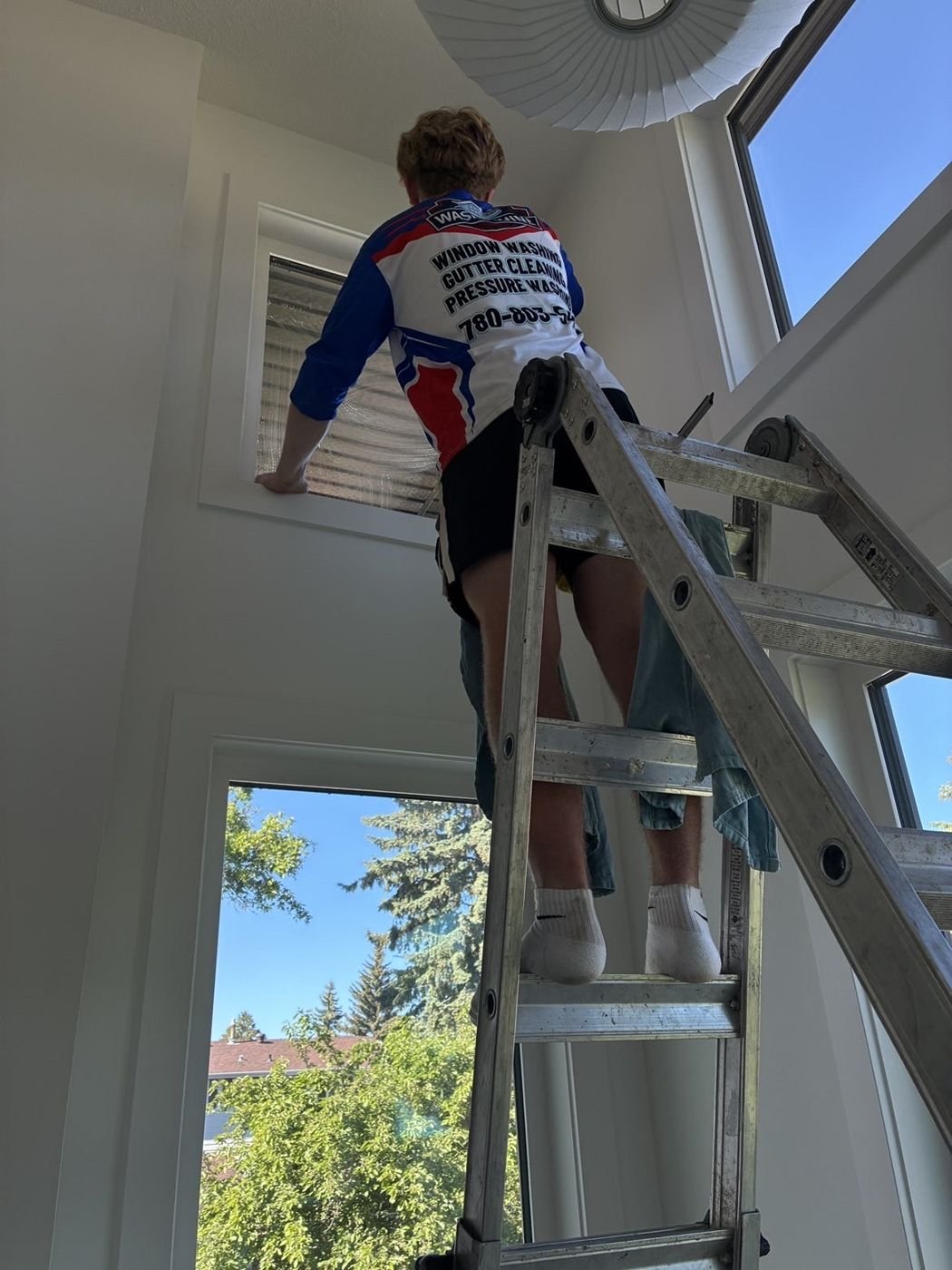 Crew member on a ladder cleaning a tall interior window